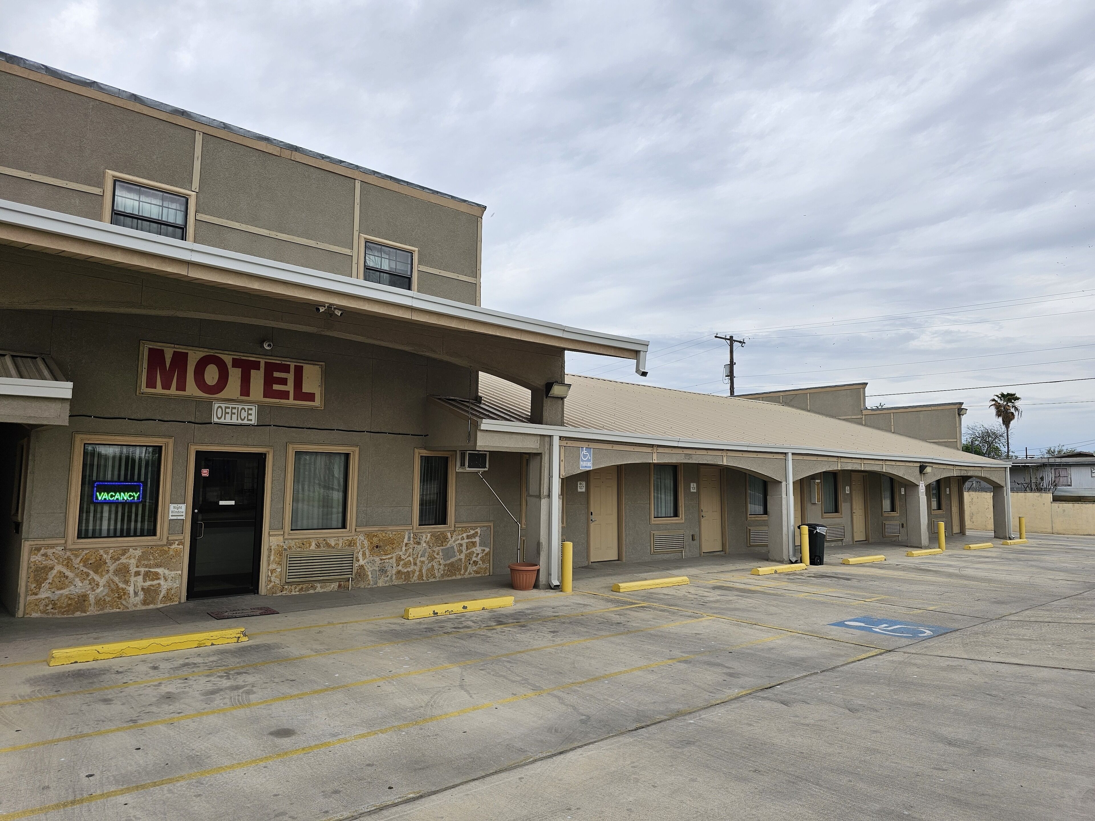A motel with a 'VACANCY' sign, a covered parking area, and a handicap-accessible entrance.