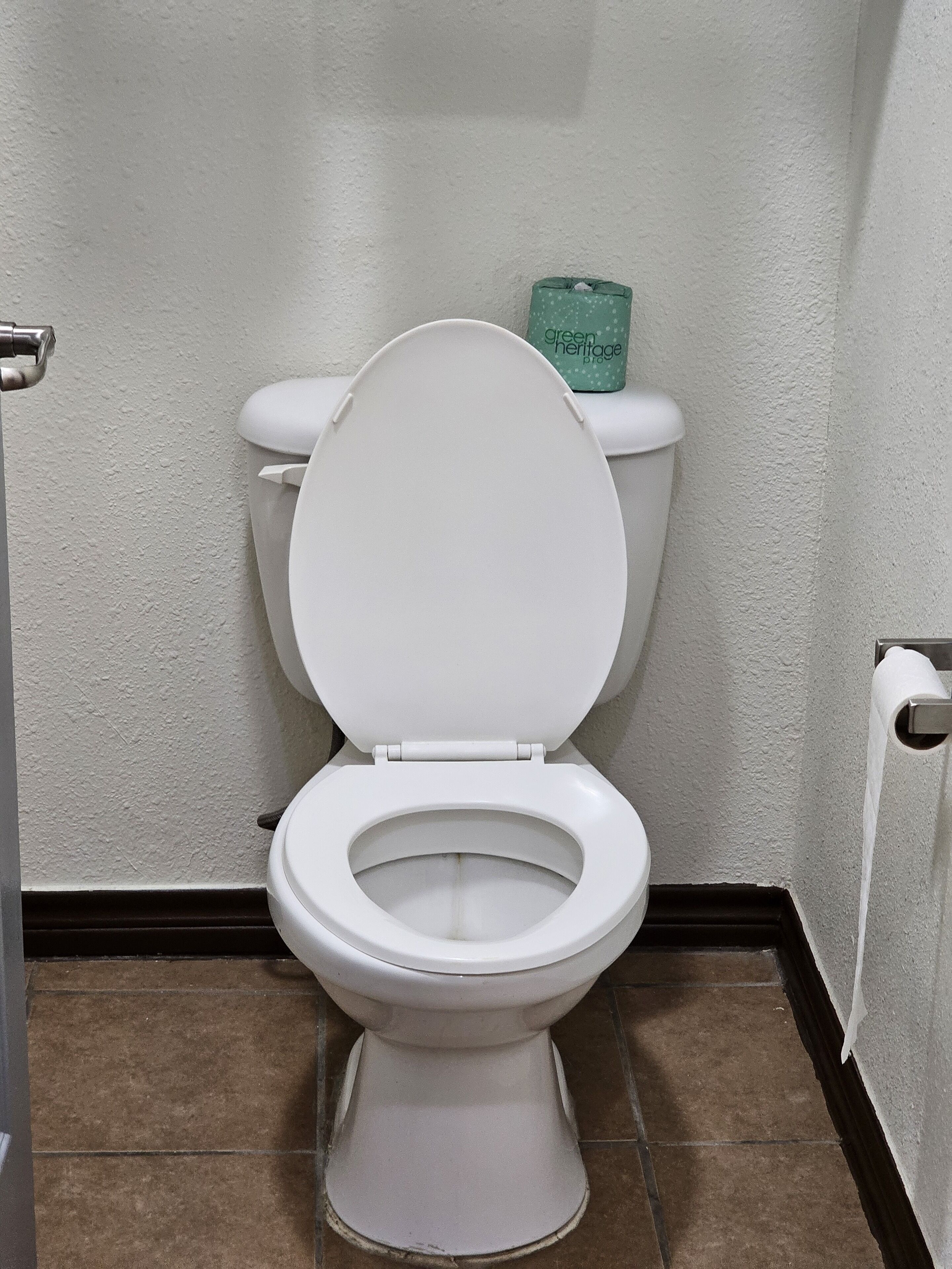 A white toilet with a closed lid in a bathroom with white walls and brown tiles.