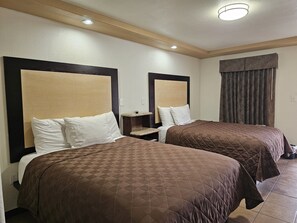 A hotel room with two beds, each with a headboard and a bedside table. - Carrizo Inn (Carrizo Springs)