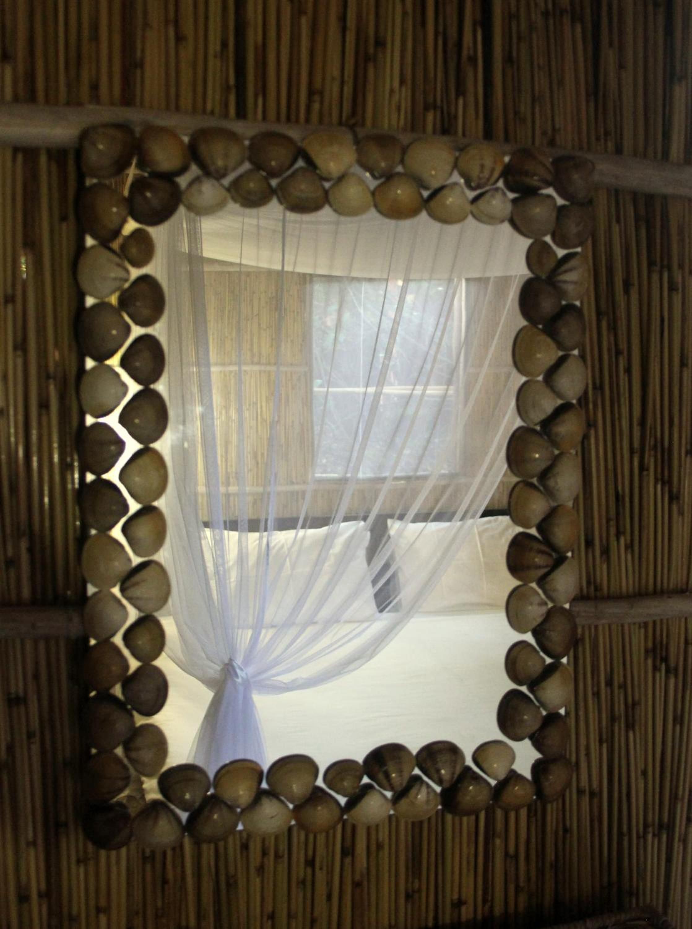 Una habitación con una cama cubierta por una cortina blanca translúcida, un espejo con marco de madera y un borde decorativo, y una pared de bambú.