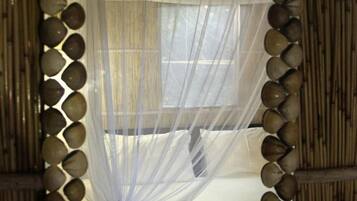 Una habitación con una cama cubierta por una cortina blanca translúcida, un espejo con marco de madera y un borde decorativo, y una pared de bambú.