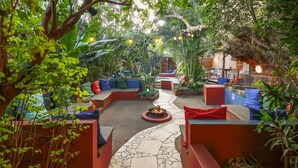 An outdoor seating area with a fire pit, surrounded by lush greenery and red and blue seating. - Gala-Gala Eco Resort (Ponta d'Ouro)