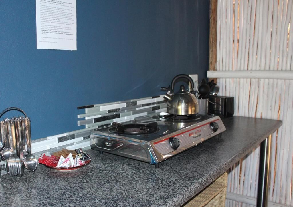 A kitchen with a portable gas stove, a kettle, and a set of utensils on the counter.