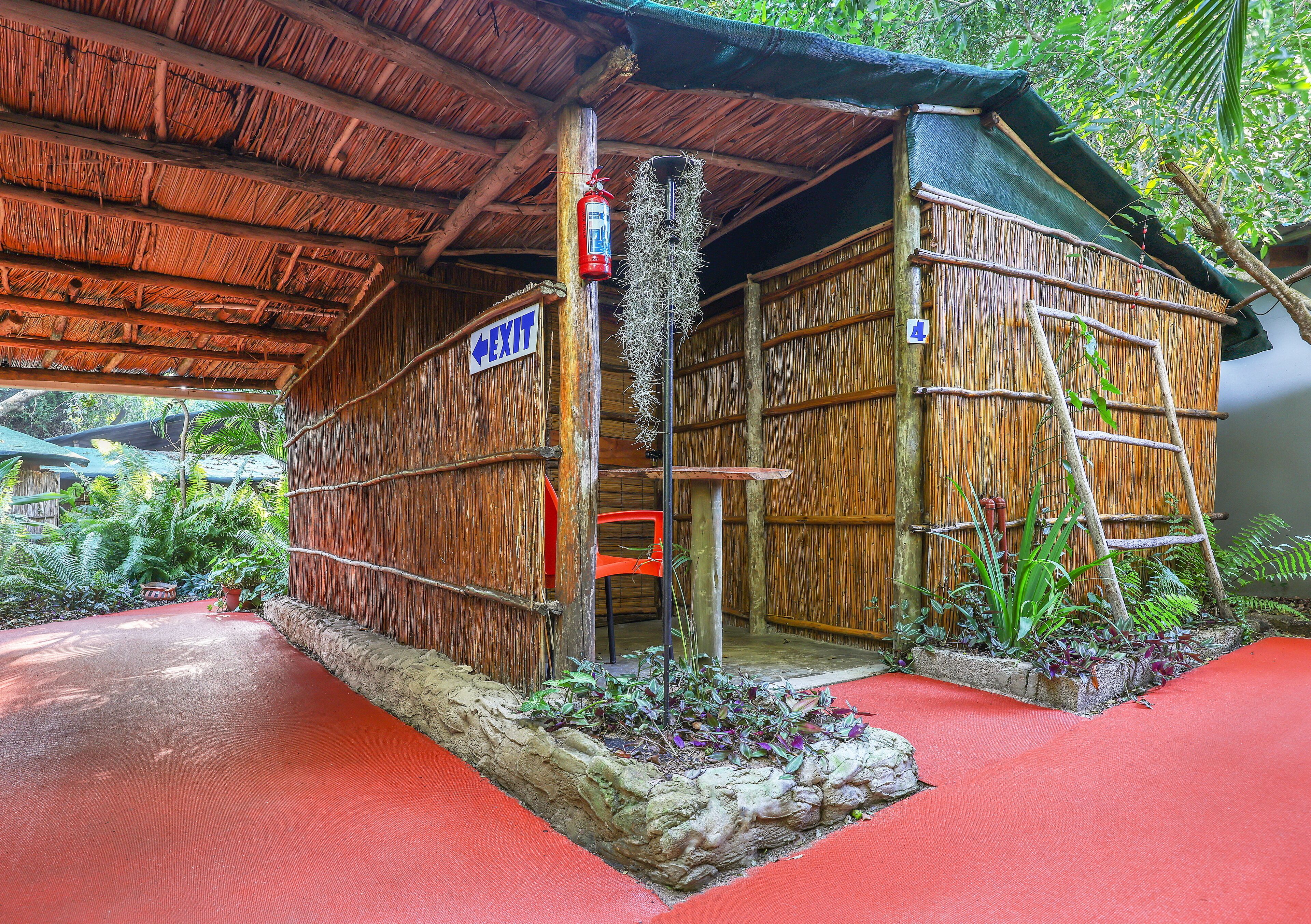 A rustic bamboo structure with a red floor, an exit sign, and a fire extinguisher.