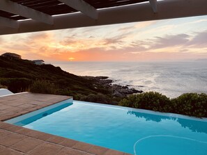 Une piscine avec vue sur l’océan au coucher du soleil.