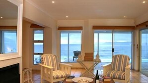 A spacious room with large windows offering ocean views, a fireplace, and two striped armchairs.