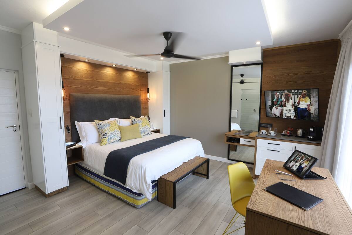A modern bedroom with a bed, bedside table, desk, chair, and a large mirror.