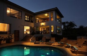 A two-story house with a swimming pool, outdoor seating, and a well-lit balcony.