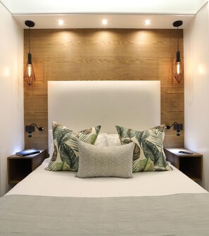 A modern bedroom with a large bed, wooden headboard, and two nightstands with wall-mounted lamps.