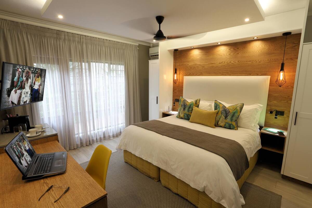 A modern hotel room with a large bed, a desk with a laptop, and a television on the wall.