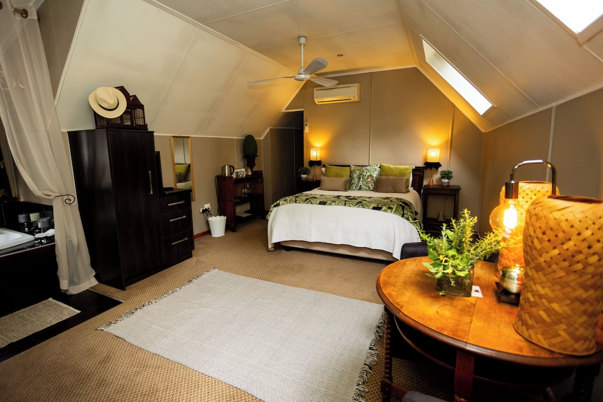 Un dormitorio con una cama, ventilador de techo, ventana y mesita de noche con lámpara.