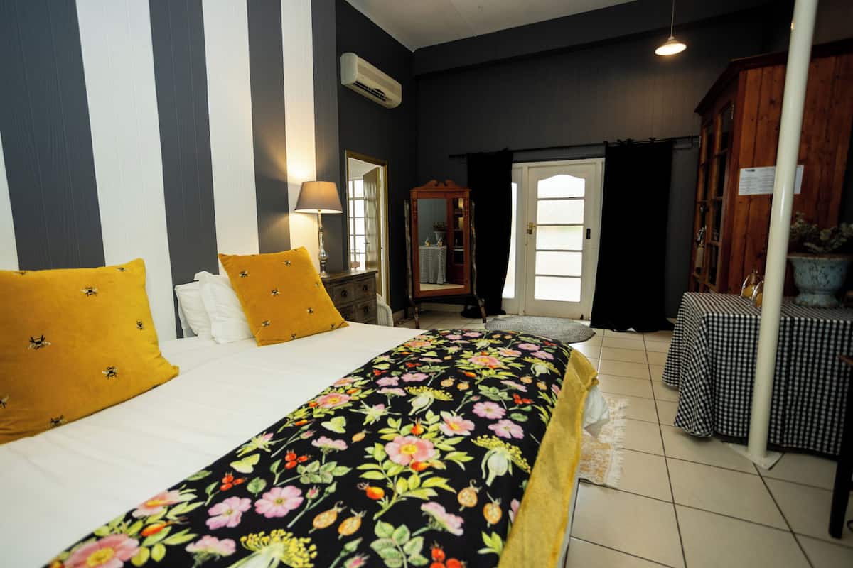 Una habitación de hotel con cama, espejo, mesa con mantel a cuadros y planta en maceta.