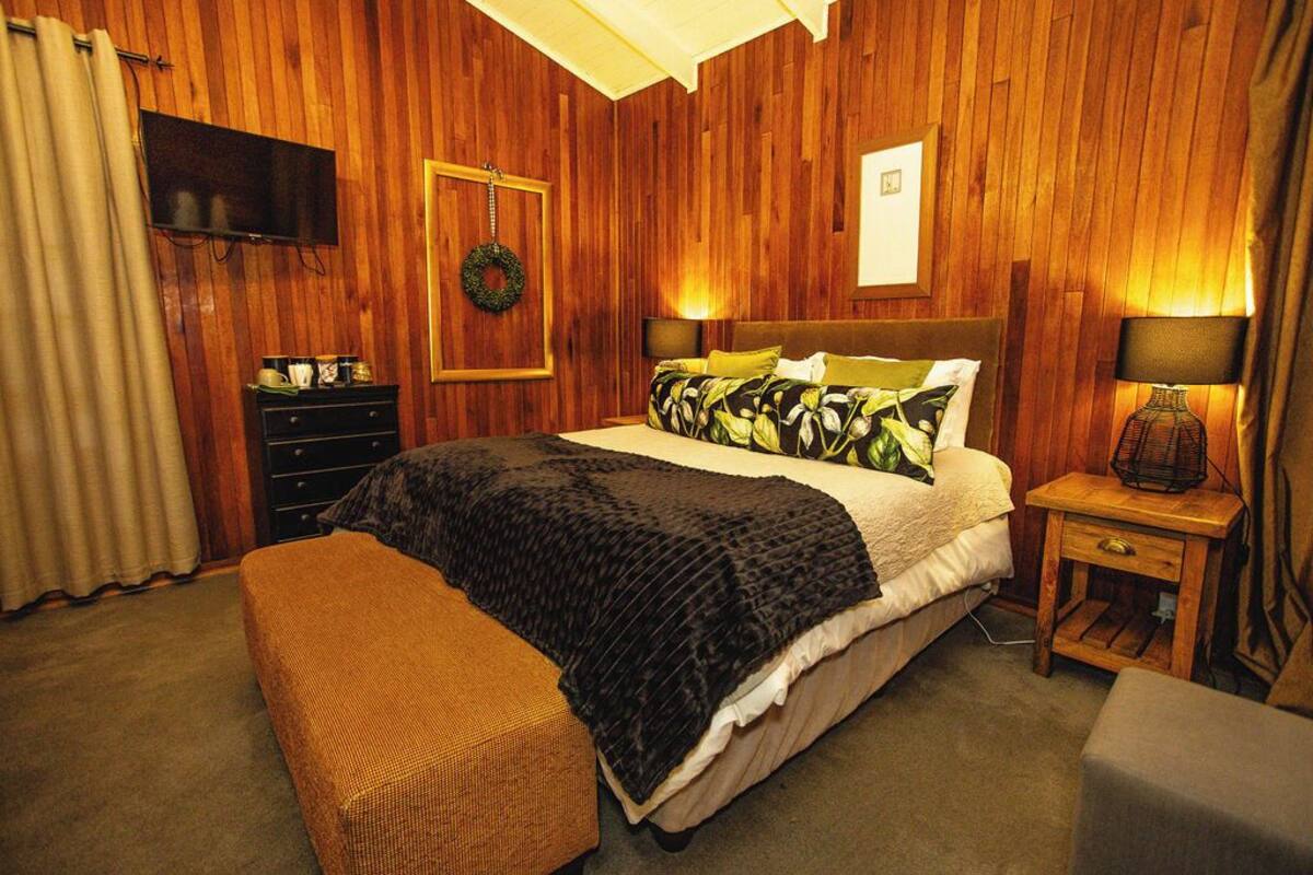 Un dormitorio con paneles de madera, una cama, mesitas de noche, un televisor y un cuadro colgado en la pared.