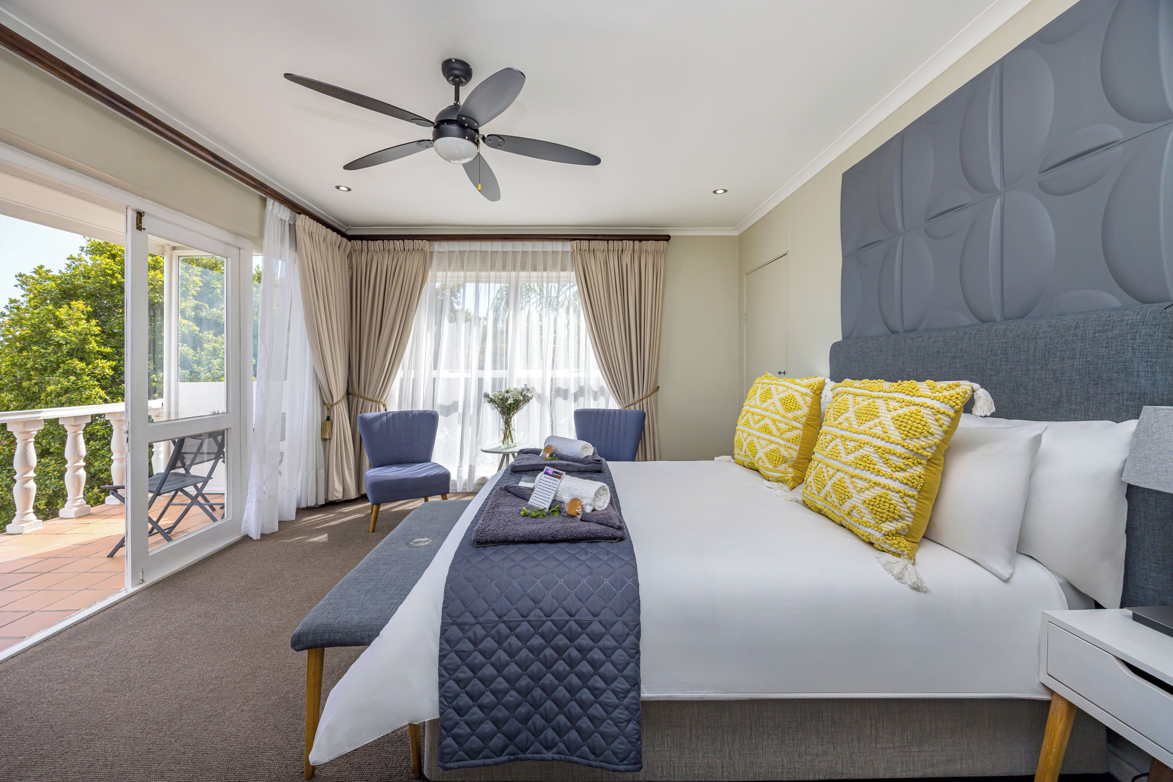 A hotel room with a bed, a desk, a chair, a ceiling fan, and a balcony.
