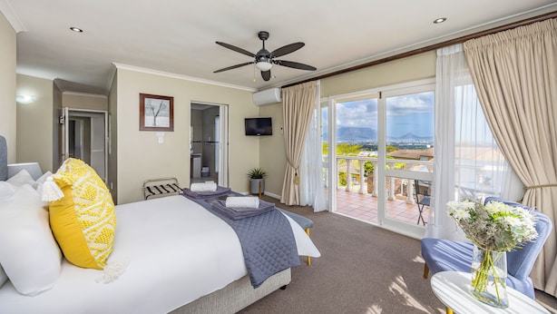 Une chambre d’hôtel avec un lit, un ventilateur de plafond, une télévision, un balcon avec vue et une table agrémentée d’un vase de fleurs.