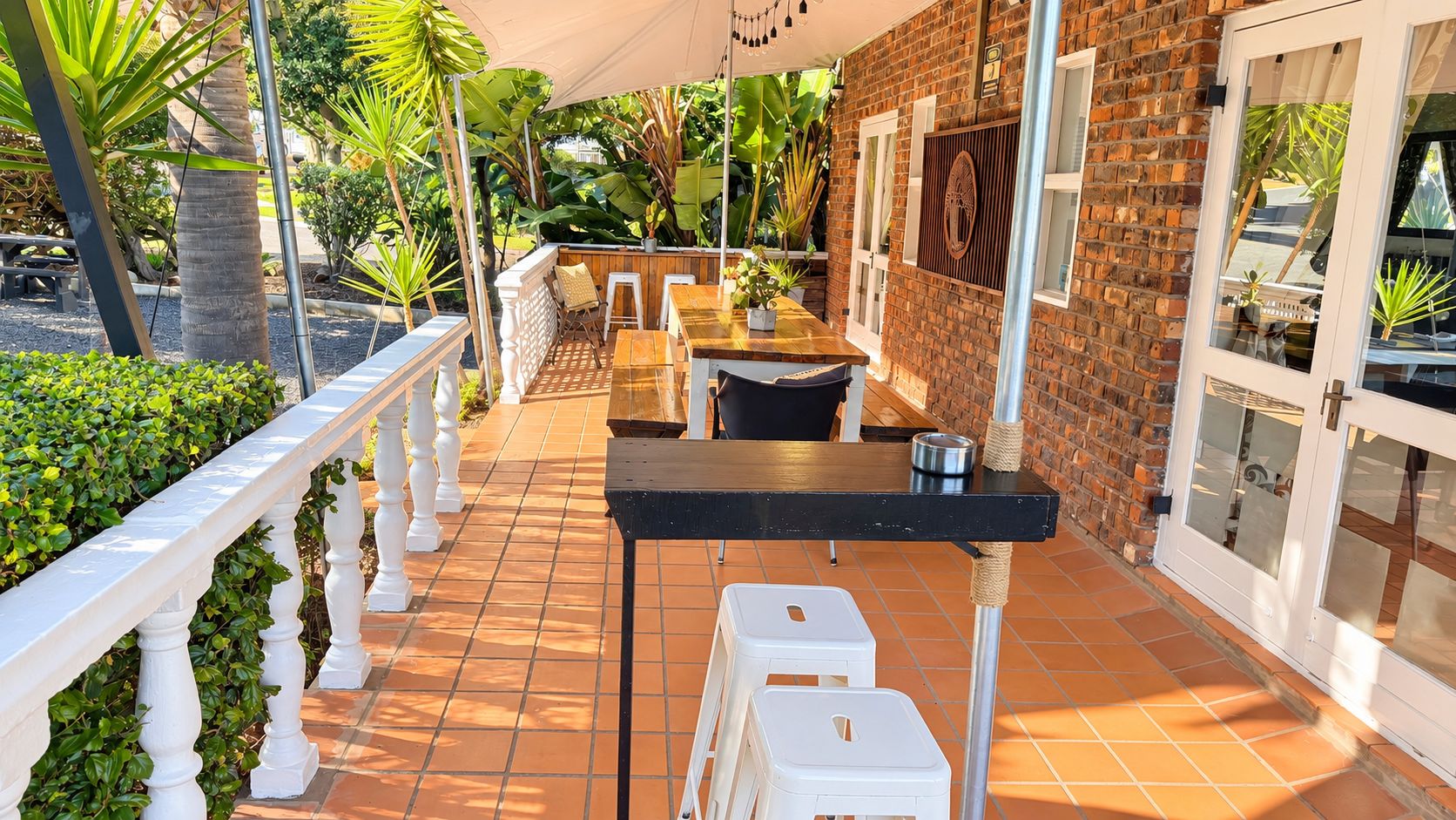 An outdoor patio with a brick wall, white railing, and a table with chairs.