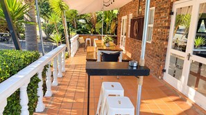 Une terrasse extérieure avec un mur en briques, une balustrade blanche et une table entourée de chaises.