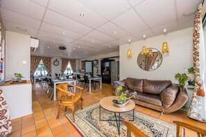 Un vaste espace de vie comprenant un canapé en cuir marron, une table basse ronde agrémentée d’une plante, et un coin repas avec une table et des chaises blanches.