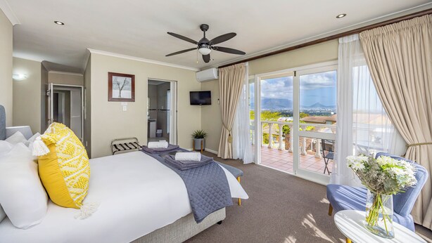 Een hotelkamer met een bed, een plafondventilator, een televisie, een balkon met uitzicht en een tafel met een bloevas.