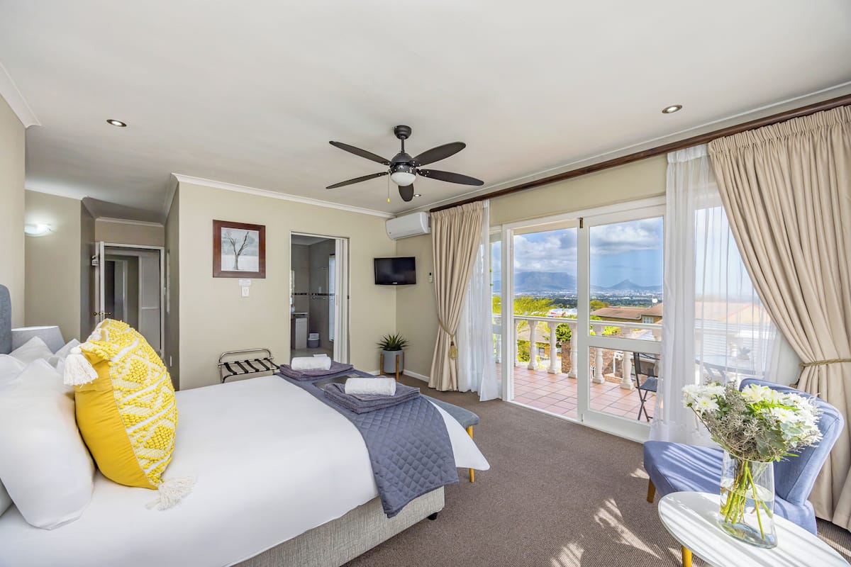 Een hotelkamer met een bed, een plafondventilator, een televisie, een balkon met uitzicht en een tafel met een bloevas.