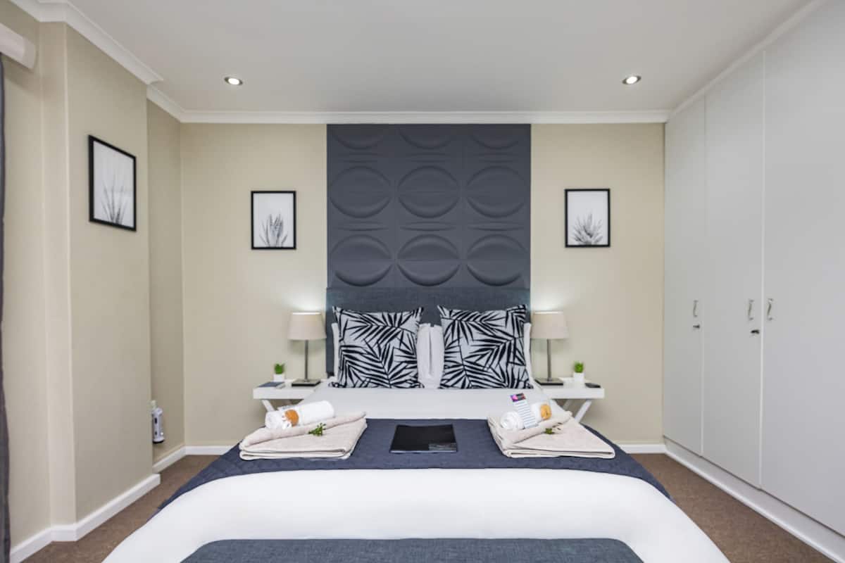 Een moderne hotelkamer met een groot bed, twee nachtkastjes, een hoofdbord met bladmotief en een garderobe.