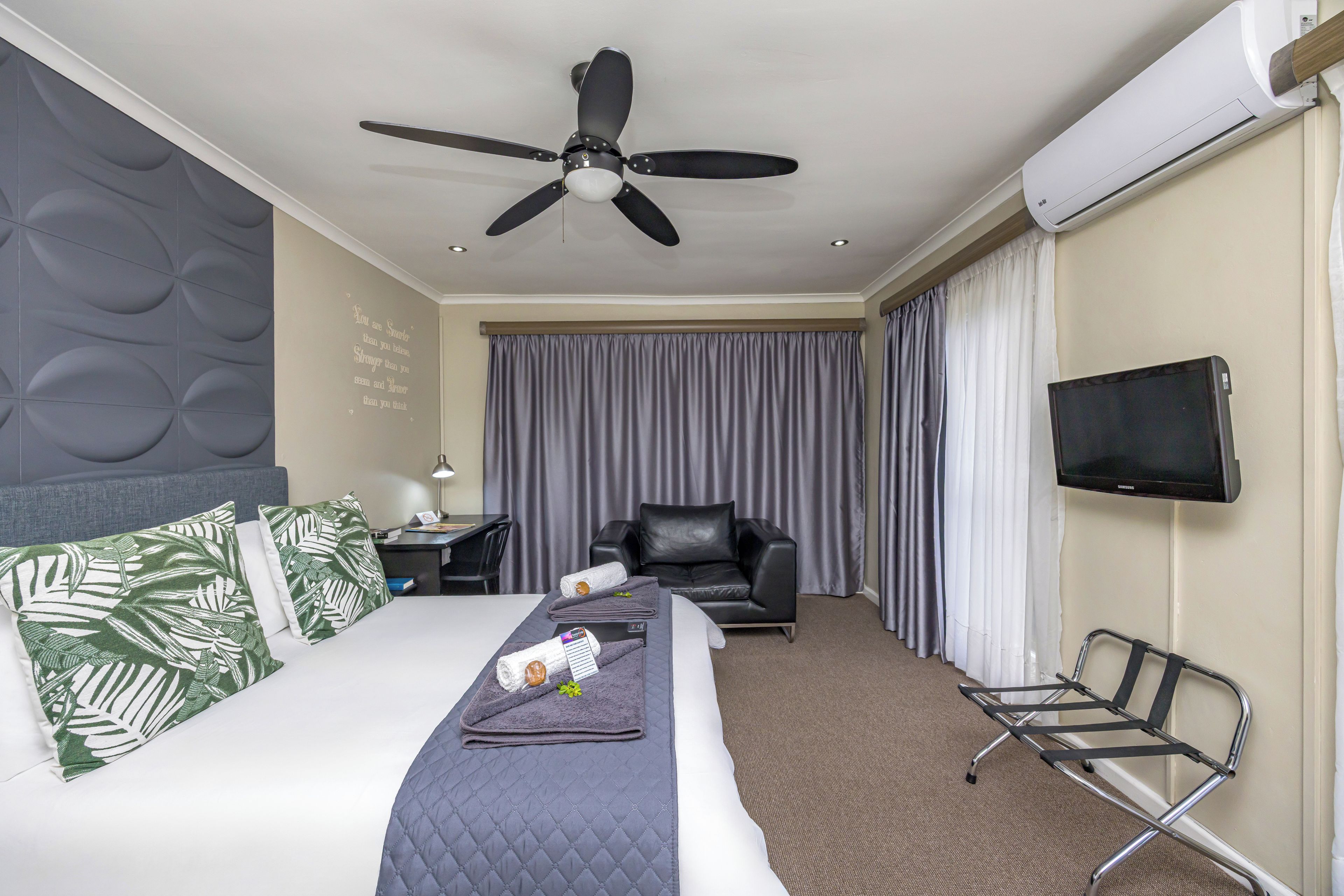 A hotel room with a bed, a desk, a chair, a TV, and a ceiling fan.