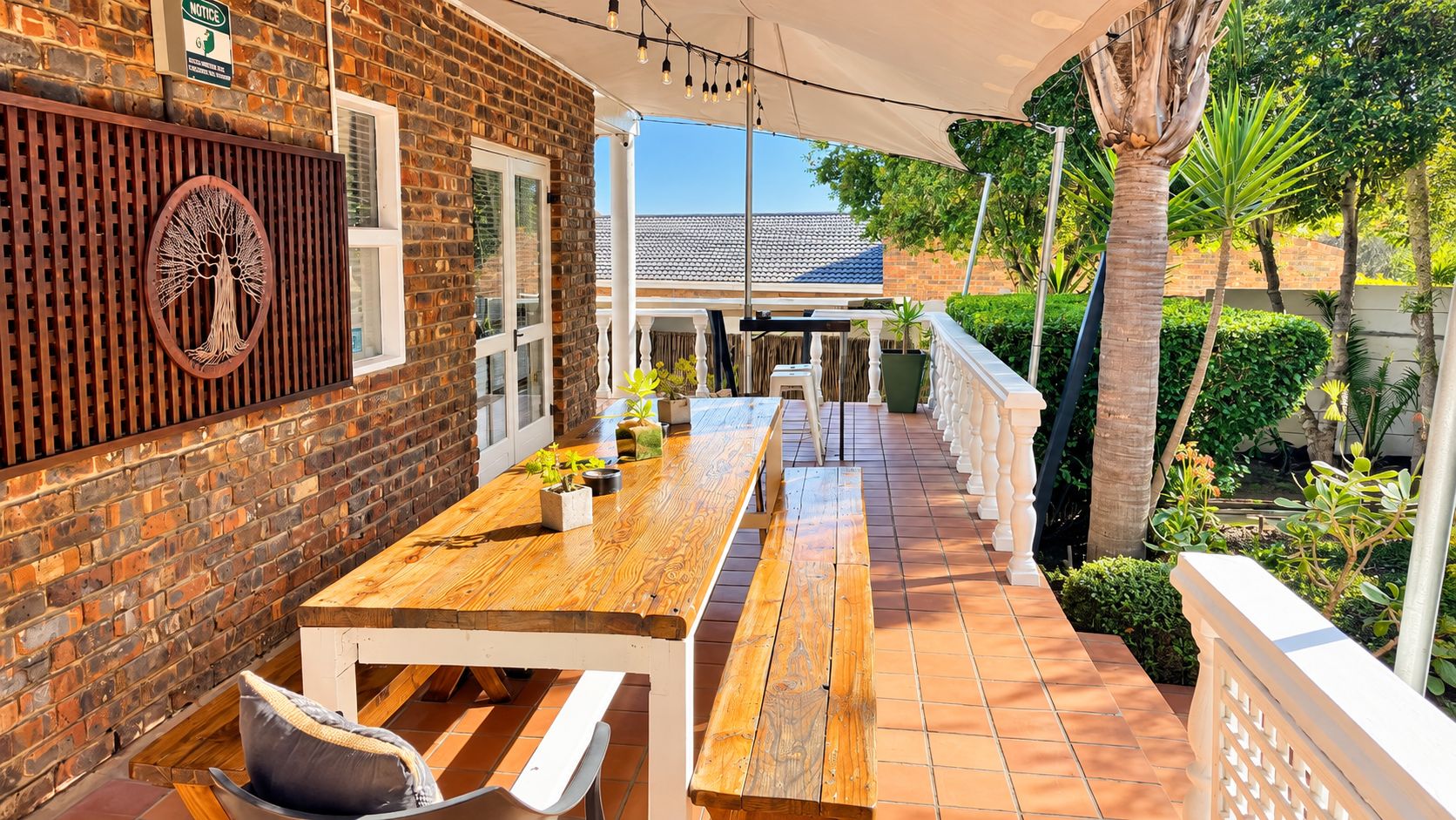 An outdoor patio with a wooden table and benches, surrounded by a brick wall and a white fence.