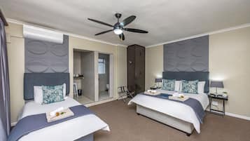 A hotel room with two beds, a ceiling fan, a minibar, and a bathroom visible through an open door.