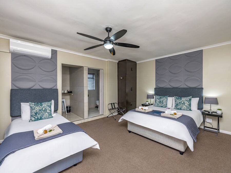 A hotel room with two beds, a ceiling fan, a minibar, and a bathroom visible through an open door.