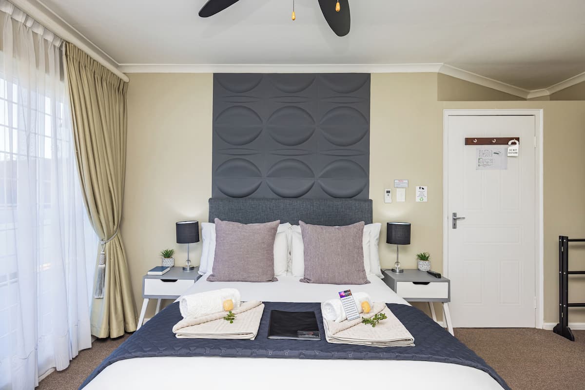 Een hotelkamer met een groot bed, twee nachtkastjes, een plafondventilator en een deur met een bordje.