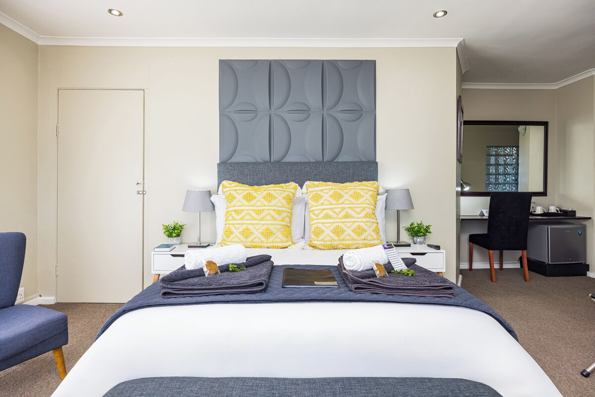 Une chambre d’hôtel avec un grand lit, deux tables de chevet, un bureau, une chaise et un miroir.