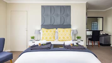 Une chambre d’hôtel avec un grand lit, deux tables de chevet, un bureau, une chaise et un miroir.