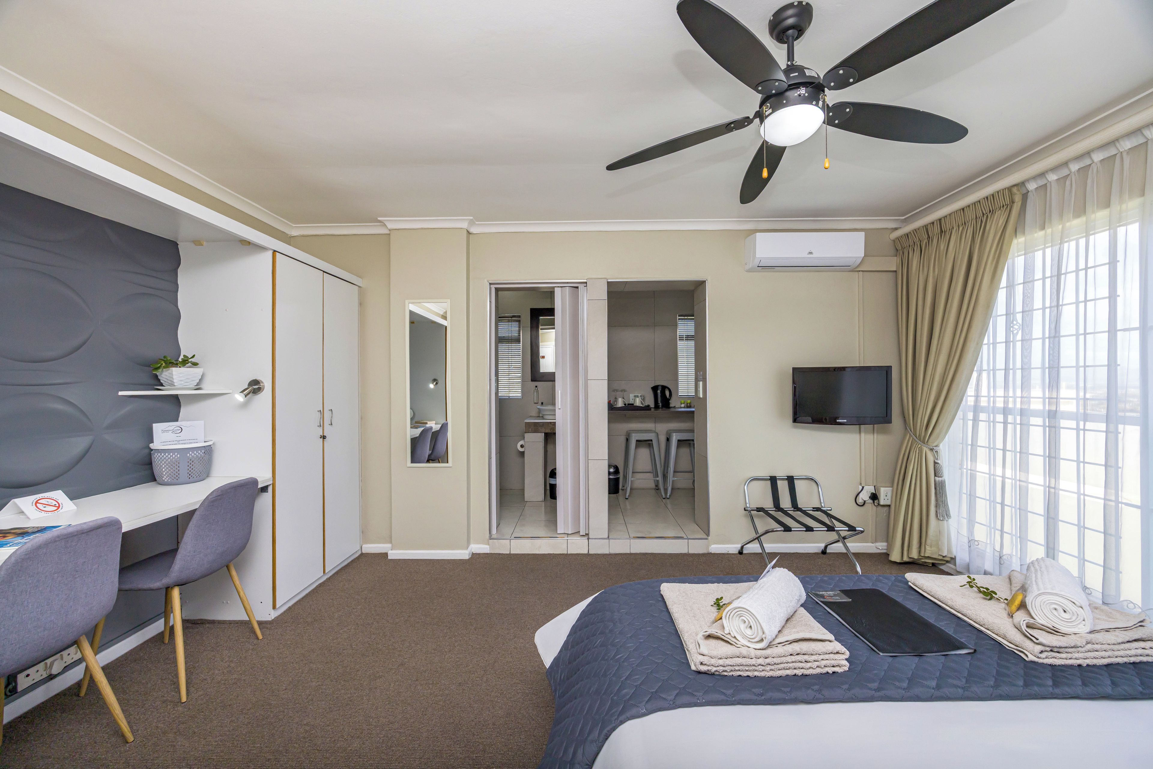 A hotel room with a bed, a desk, a chair, a TV, and a ceiling fan.