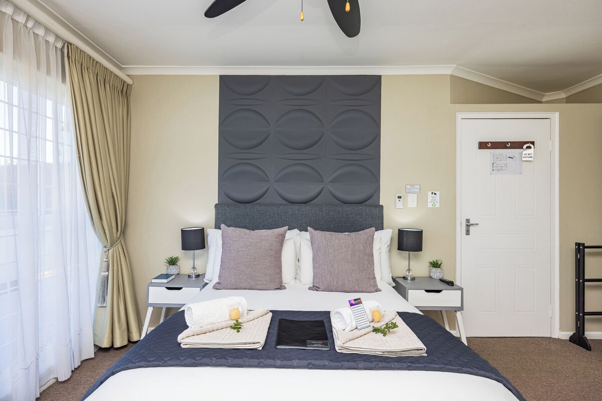 Une chambre d’hôtel avec un grand lit, deux tables de chevet, un ventilateur de plafond et une porte avec une pancarte.
