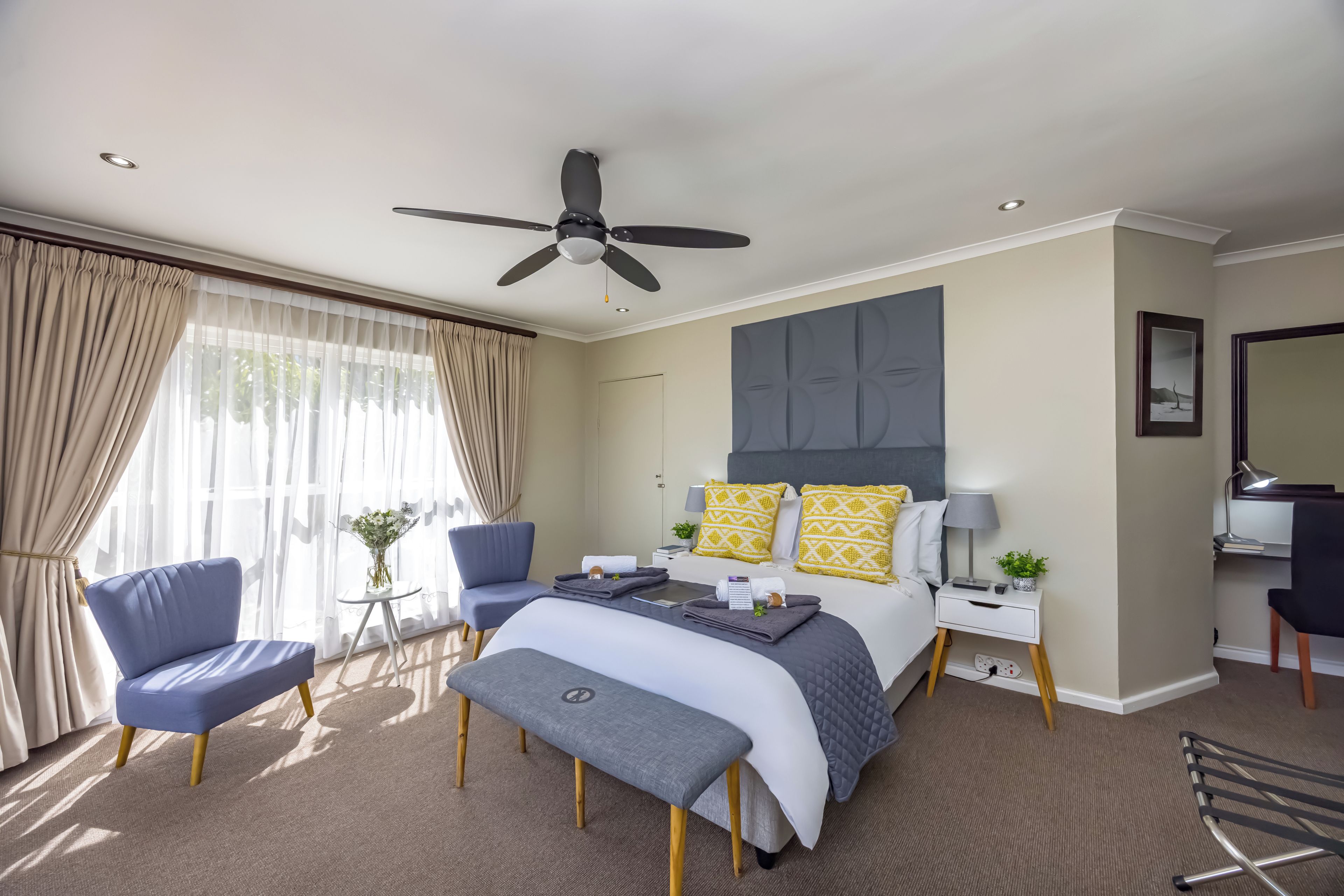Ein modernes Hotelzimmer mit einem Bett, zwei Sesseln, einem Schreibtisch und einem Deckenventilator.