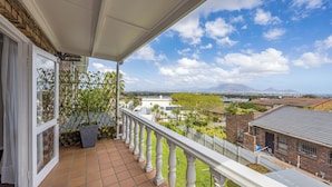 Un balcon donnant sur un quartier résidentiel, avec une balustrade blanche et une porte à panneaux de verre.