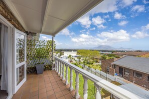 Un balcon donnant sur un quartier résidentiel, avec une balustrade blanche et une porte à panneaux de verre.