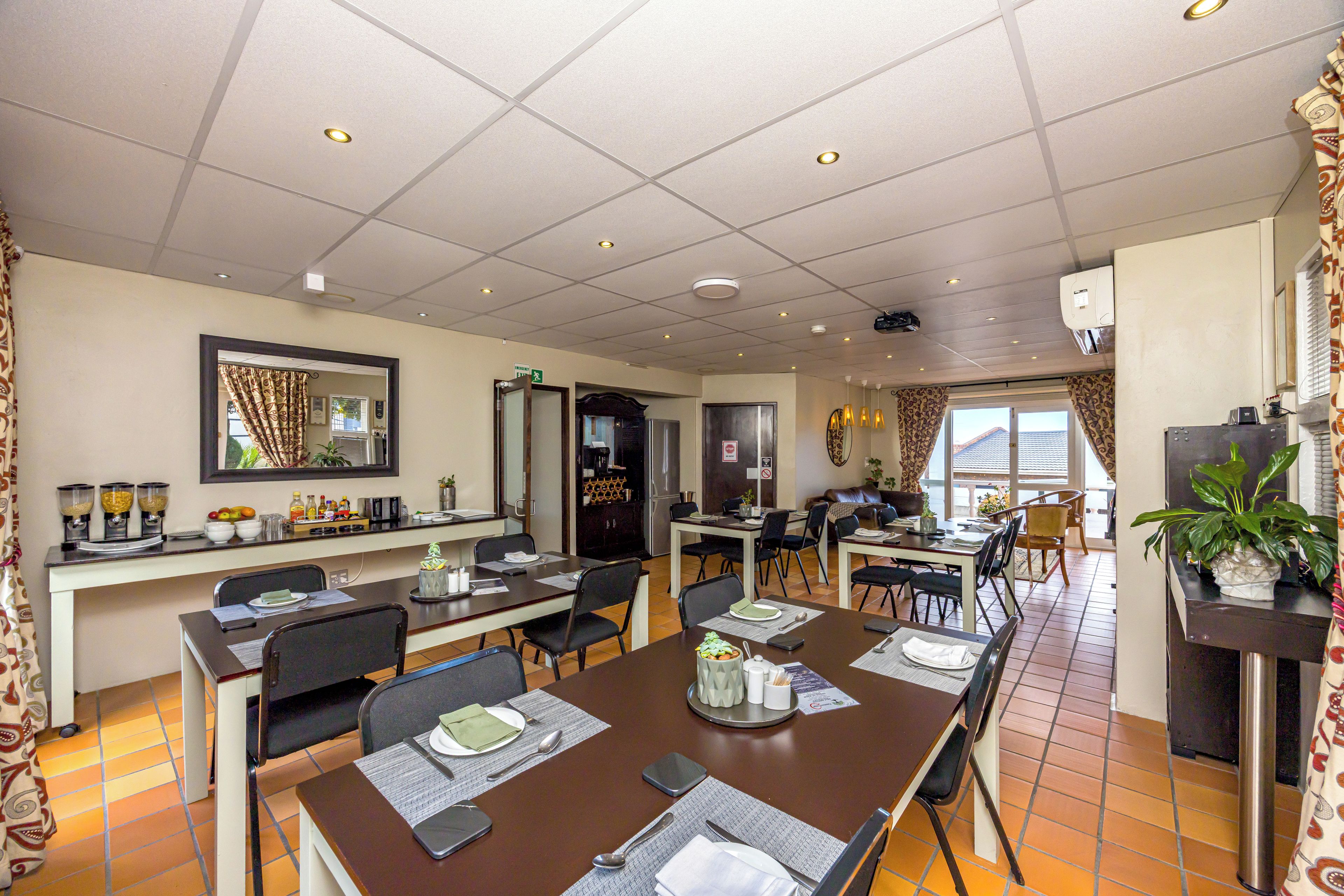 Un comedor de hotel con varias mesas, sillas y una zona de cocina al fondo.