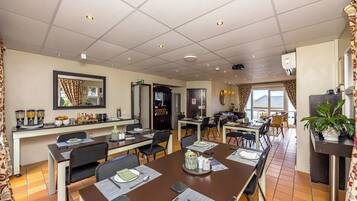 Un comedor de hotel con varias mesas, sillas y una zona de cocina al fondo.