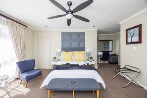 Une chambre d’hôtel équipée d’un lit, d’un bureau, d’une chaise, d’un ventilateur de plafond et d’une fenêtre avec des rideaux.