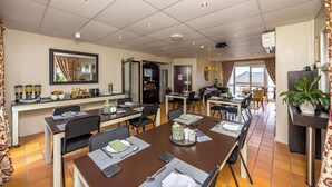 Een restaurantgedeelte in een hotel, met meerdere tafels, stoelen en een zichtbare keuken op de achtergrond.