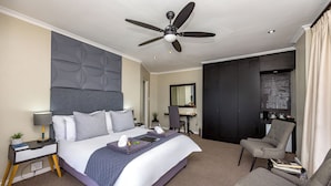 Een moderne hotelkamer met een groot bed, een bureau, een stoel en een plafondventilator.