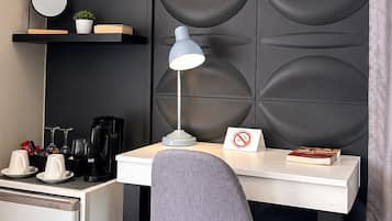 Habitación de hotel compacta con escritorio, silla, equipo de aire acondicionado y un panel decorativo en la pared.