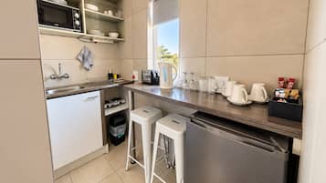 A compact kitchen with a microwave, toaster, kettle, and coffee maker. There are two stools and a trash bin.