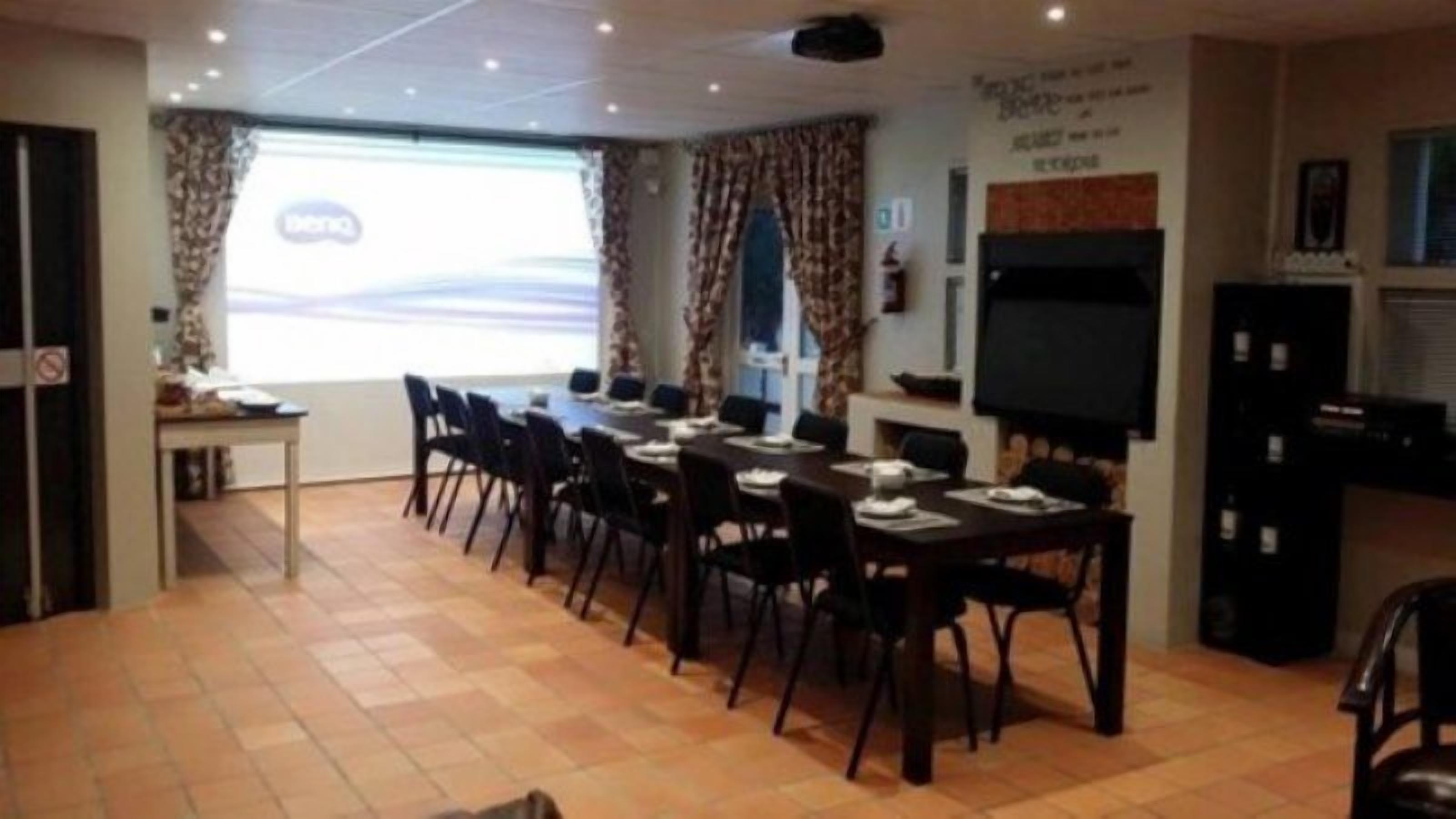 Un salón de conferencias con una larga mesa, sillas, una pantalla de proyector y una televisión.