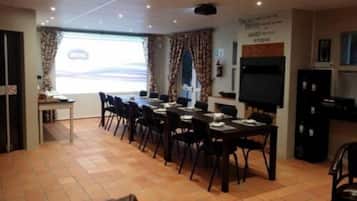 A conference room with a long table, chairs, a projector screen, and a television.