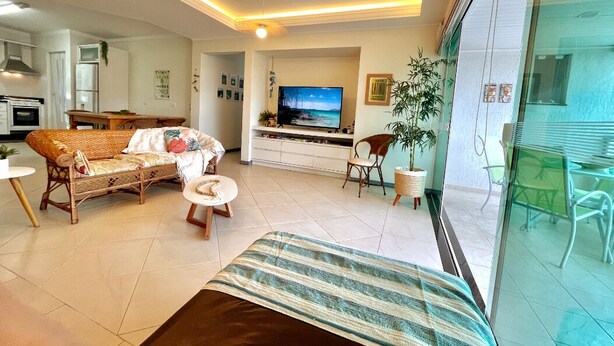 A modern living room with a sofa, a television, and a dining area. - Apartamento do Sol (Bombinhas)