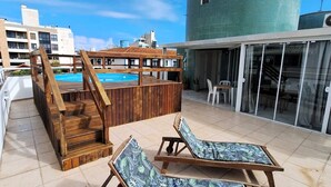 A rooftop pool area with wooden loungers and a large cylindrical water tank. - Apartamento do Sol (Bombinhas)