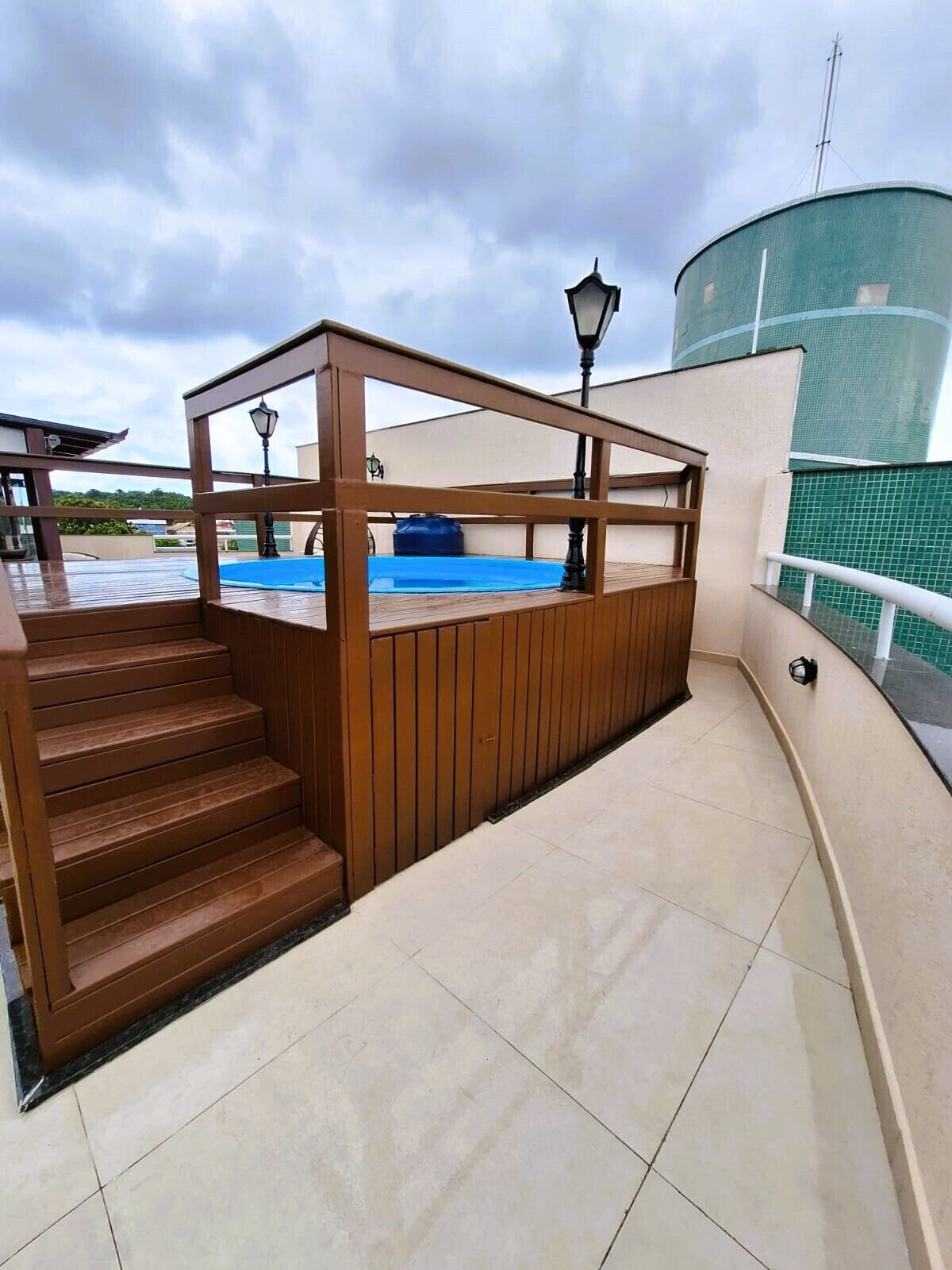 A rooftop terrace with a wooden deck, a blue pool, and a water tank in the background.