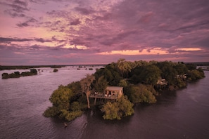 Ein schwimmendes Haus mit Terrasse und Sitzgelegenheiten, umgeben von Wasser und Bäumen.